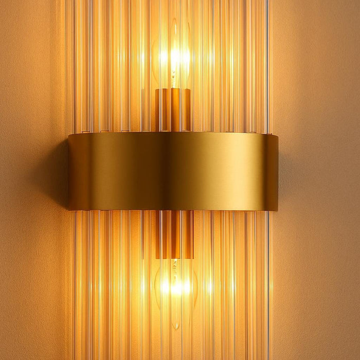 A close-up shot of the Addo Wall Lamp highlighting its high-quality matte gold material, elongated central bar intersected by a shorter horizontal element, with two E14 bulbs emitting a cozy, inviting light, set against a neutral textured background.