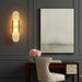 A lifestyle scene showing the sconce illuminating a stylish hallway with elegant décor, emphasizing the elongated, rounded silhouette and inviting glow, with a focus on the contrast between the gold finish and the surrounding décor.