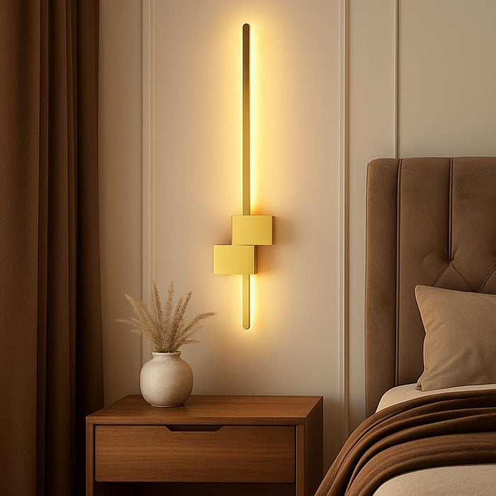 A lifestyle scene showing the Arlo Gold Wall Light installed above a contemporary bedside table in a luxurious bedroom, with rich textiles and natural wood elements, emphasizing its elegant geometric accents and warm white glow.