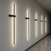 A series of Dario LED wall lights installed along a large, textured hallway wall, creating a dynamic, artful lighting installation that emphasizes the minimalist aesthetic.